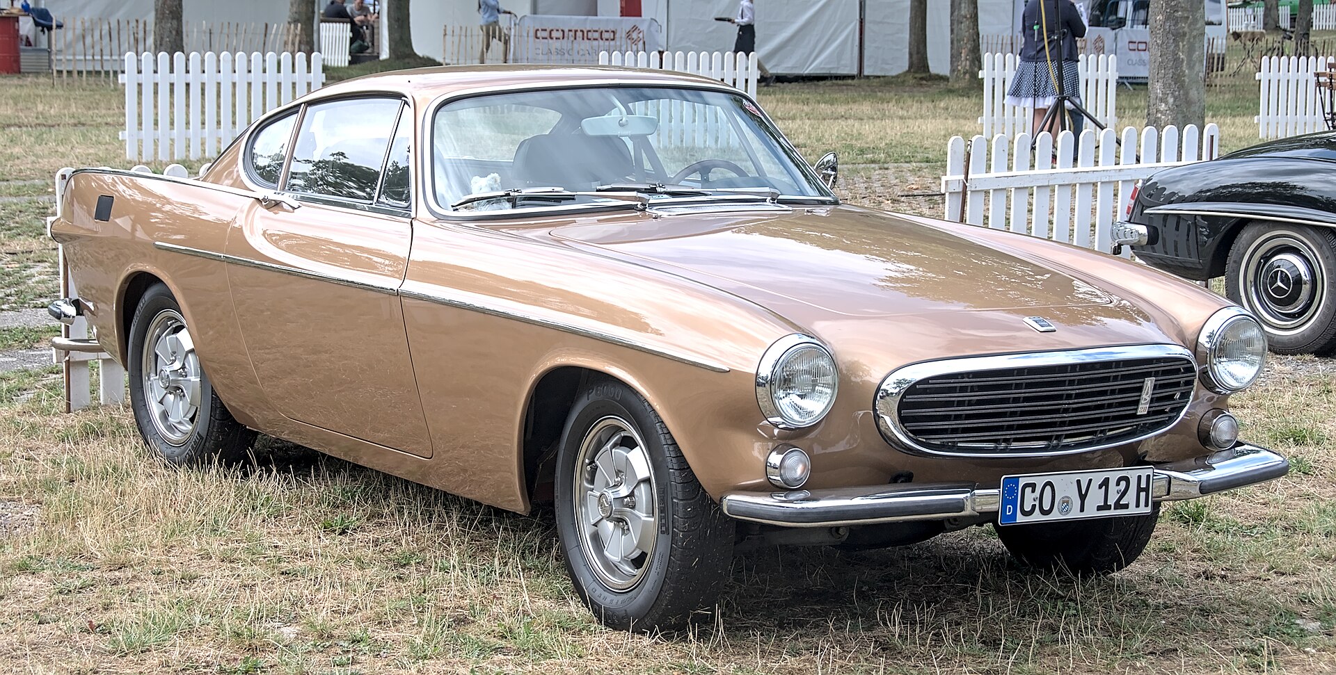 Front three-quarter view of a bronze Volvo P1800 Coupe